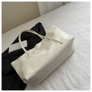 Detail of minimalist beige tote bag with slim shoulder straps on textured fabric