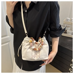 Detail of white drawstring bucket bag with colorful beaded handle and logo print