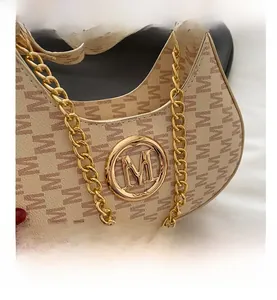 Detail of beige shoulder bag with letter M texture and gold metal logo and chain