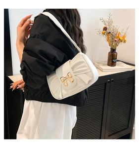 Close-up of white pleated shoulder bag with golden bow-knot buckle on a model