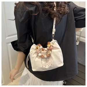 Detail of cream drawstring bucket bag with marble bead handle and bear logo print