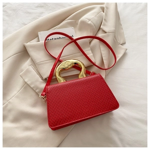 Detail of red textured bag with artistic gold metal handle on a white blazer background