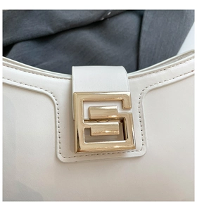 Close-up of golden geometric buckle and fine leather texture on an off-white shoulder bag