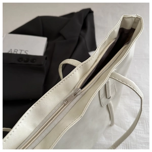 Detail of off-white tote bag with silver zipper closure and pebbled leather texture