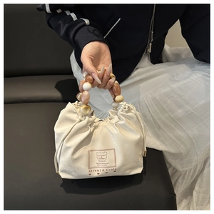 Detail view of the beaded handle and drawstring closure on the stylish beige handbag