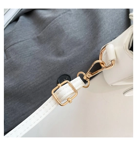 Macro view of gold-tone metal buckle and lobster clasp on white faux leather shoulder strap