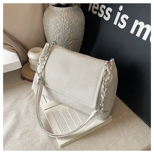 Close-up of cream woven fabric texture and metal chain strap on a chic shoulder bag