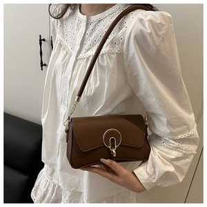 Detail of a brown leather shoulder bag featuring a round golden metallic lock on a flap