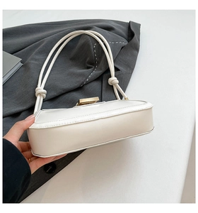 Detailed view of white leather shoulder bag featuring gold clasp and knot strap accents