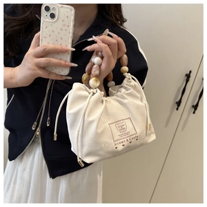 Detail of beaded handle and bear print on off-white drawstring crossbody bag