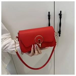 Détail d'un sac bandoulière en cuir rouge avec fermoir doré rond et chaîne