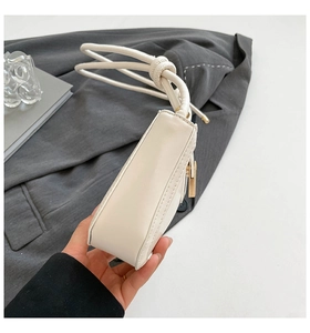 Close-up of cream leather shoulder bag featuring unique knotted strap and gold hardware
