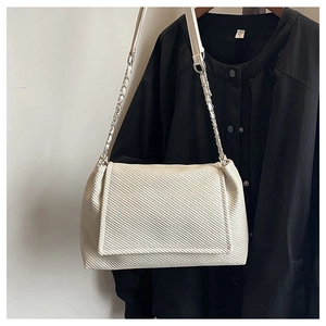 Macro detail of creamy twill fabric texture and metallic chain strap on a tote bag