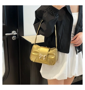 Detail of a metallic gold shoulder bag featuring a prominent bow decoration on a model