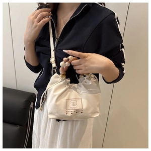 Détail du sac seau en toile blanche avec poignée en perles marbrées et bandoulière