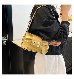 Detail of metallic gold shoulder bag featuring pleated texture and metal bow clasp
