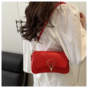 Detail of red crossbody bag featuring gold circular magnetic clasp and metal chain strap
