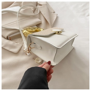 Detailed close-up of white leather crossbody bag with woven texture and gold metal handle