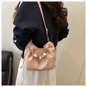 Pink drawstring bucket bag with marble beaded handle shown as a stylish crossbody bag