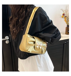 Side view of champagne gold baguette bag with a metallic finish and bow detail