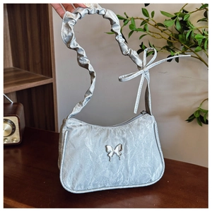 Close-up of metallic silver pleated underarm bag with butterfly charm and ruffled strap