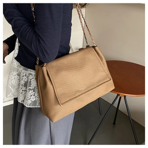 Detail of a brown textured shoulder bag featuring an elegant metal chain strap design