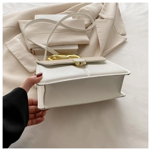 Detail view of the gusseted side structure and gold handle on this white crossbody bag