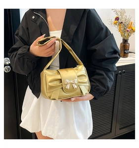 Close-up of golden metallic bow underarm bag with glossy finish and snap closure
