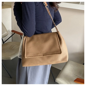 Detail of brown woven texture tote bag with metal chain strap on model shoulder