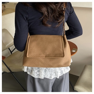 Detailed close-up of brown twill woven flap bag with stylish metal chain strap
