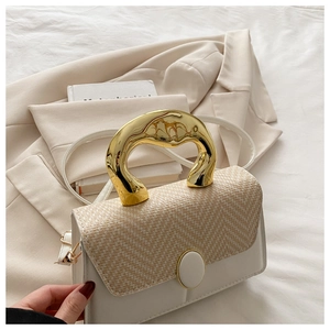 Detail of elegant gold metal handle and woven texture on white leather handbag
