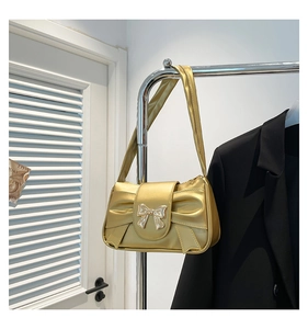Close-up of golden pleated underarm bag with metallic bow design and silver buckle