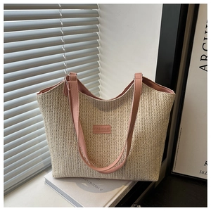 Close-up of beige woven straw tote bag featuring pink leather strap and fashion label