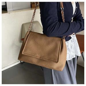 Detail of a brown textured crossbody bag with silver metal chain and flap cover