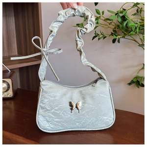 Close-up of light green pleated underarm bag with silver butterfly charm and ruffled strap