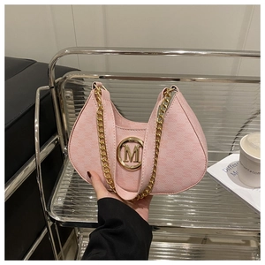 Detail of pink half-moon bag featuring a gold metal M logo and stylish chain strap
