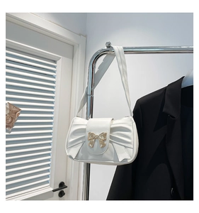 Detail of white pleated handbag with golden butterfly clasp and bow design