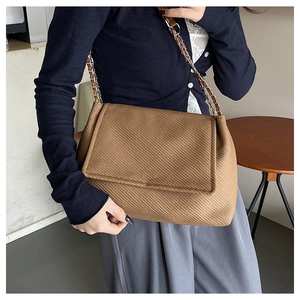 Close-up of brown woven crossbody bag featuring leather and metal chain strap details
