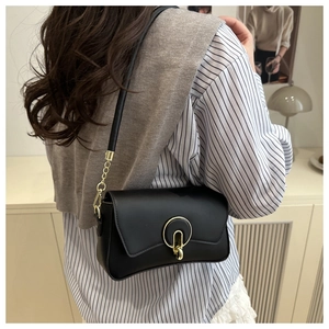 Detail of a black faux leather crossbody bag with a stylish gold circular metal buckle