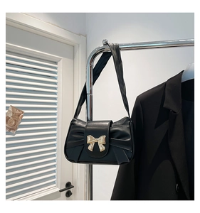 Detail of a black pleated shoulder bag featuring a vintage golden bow metal clasp