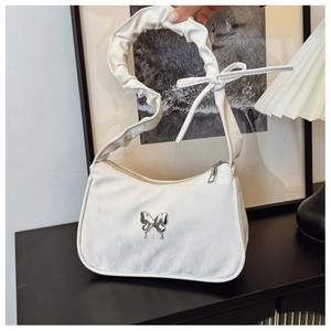 Detailed shot of white pleated shoulder bag with silver butterfly and bow accent