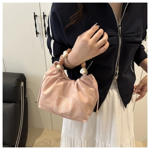 Close-up of pink drawstring handbag featuring amber beaded handles and logo detail