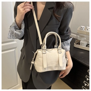 Vue détaillée du sac Boston crème avec lettrage embossé porté par un mannequin