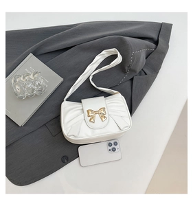 Detail of white pleated underarm bag with a golden bow buckle on the front flap