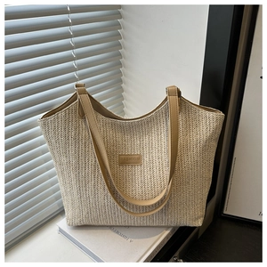 Detail of woven straw tote bag featuring khaki leather strap and fashion leather patch