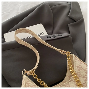 Detail of beige monogram underarm bag with gold chain strap on a grey blazer