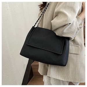 Detail of black crossbody bag with textured fabric and metal chain leather strap