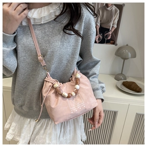 Pink bucket bag with colorful resin beaded handle and logo detail in casual setting