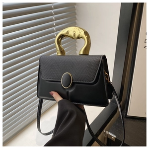 Close-up of black crossbody bag with gold artistic handle and textured flap held by hand