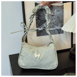Detail of light green pleated handbag featuring silver butterfly logo and ruffled handle
